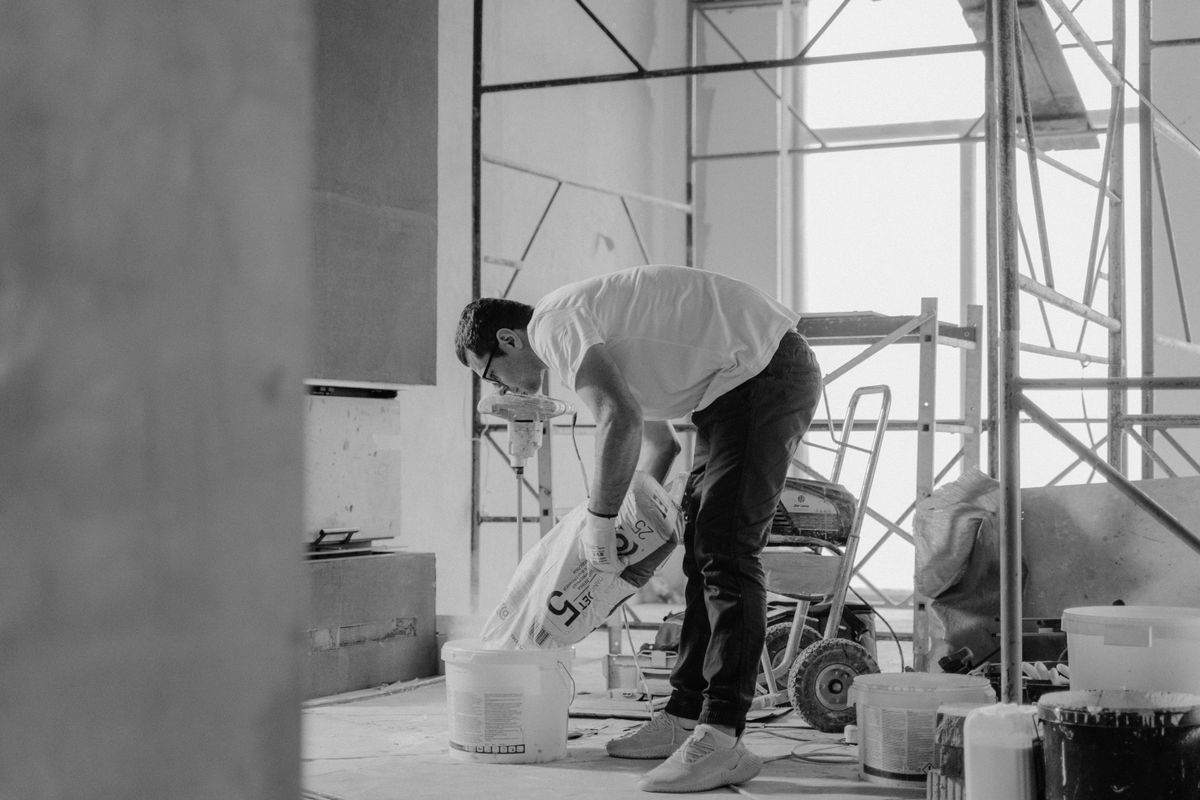 A worker mixing material on a renovation site with scaffolding