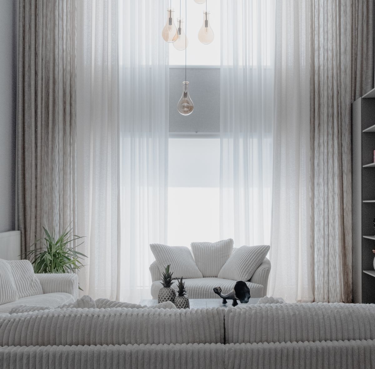 A bright minimalist living room with white sofas and tall curtains