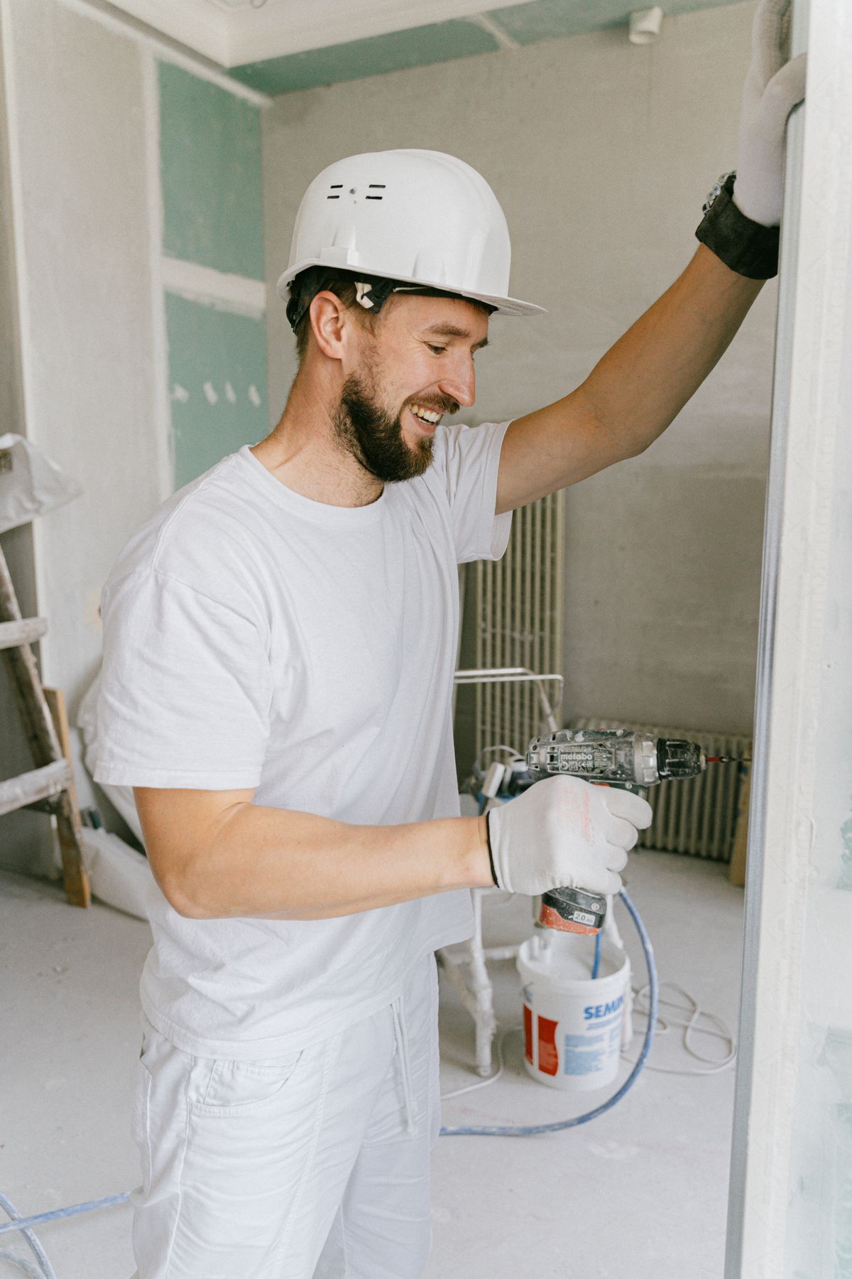 A worker in a white hard hat holding spray equipment during a renovation