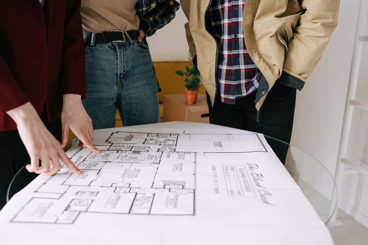 A group standing around a table pointing at a floor plan