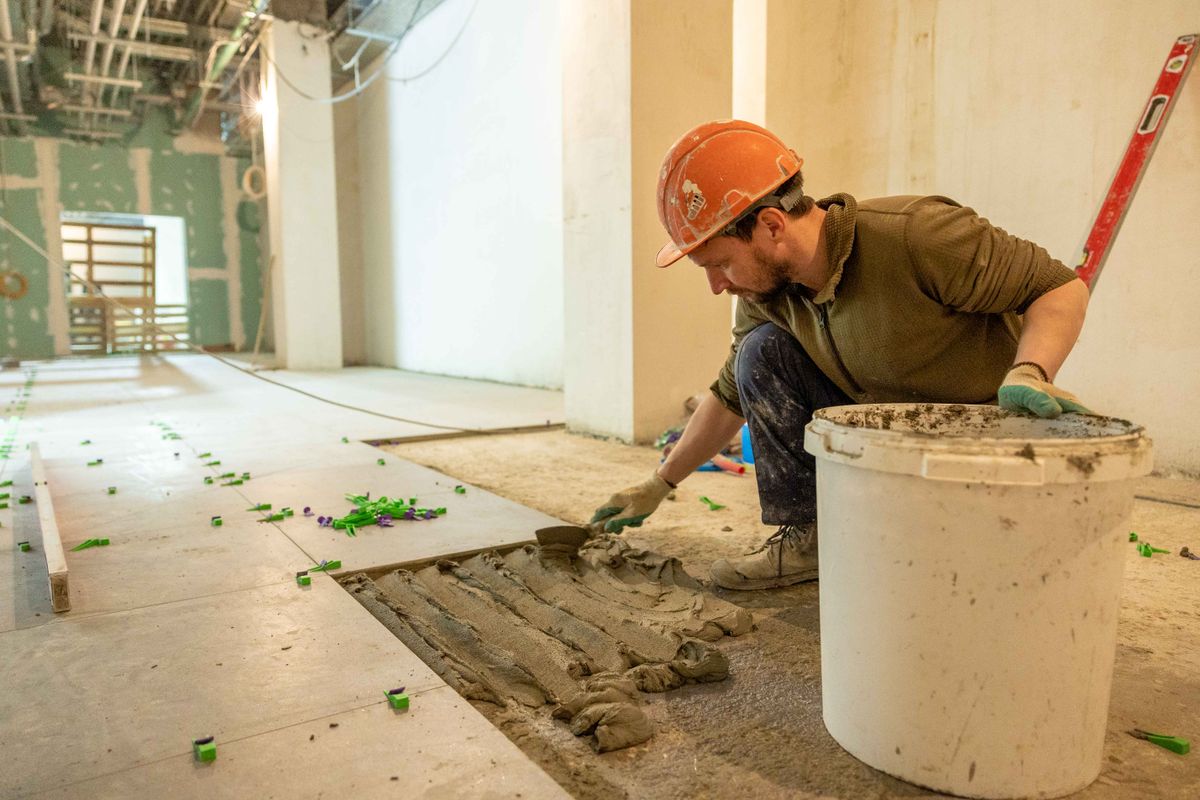 A worker in an orange hard hat laying floor tile during a renovation