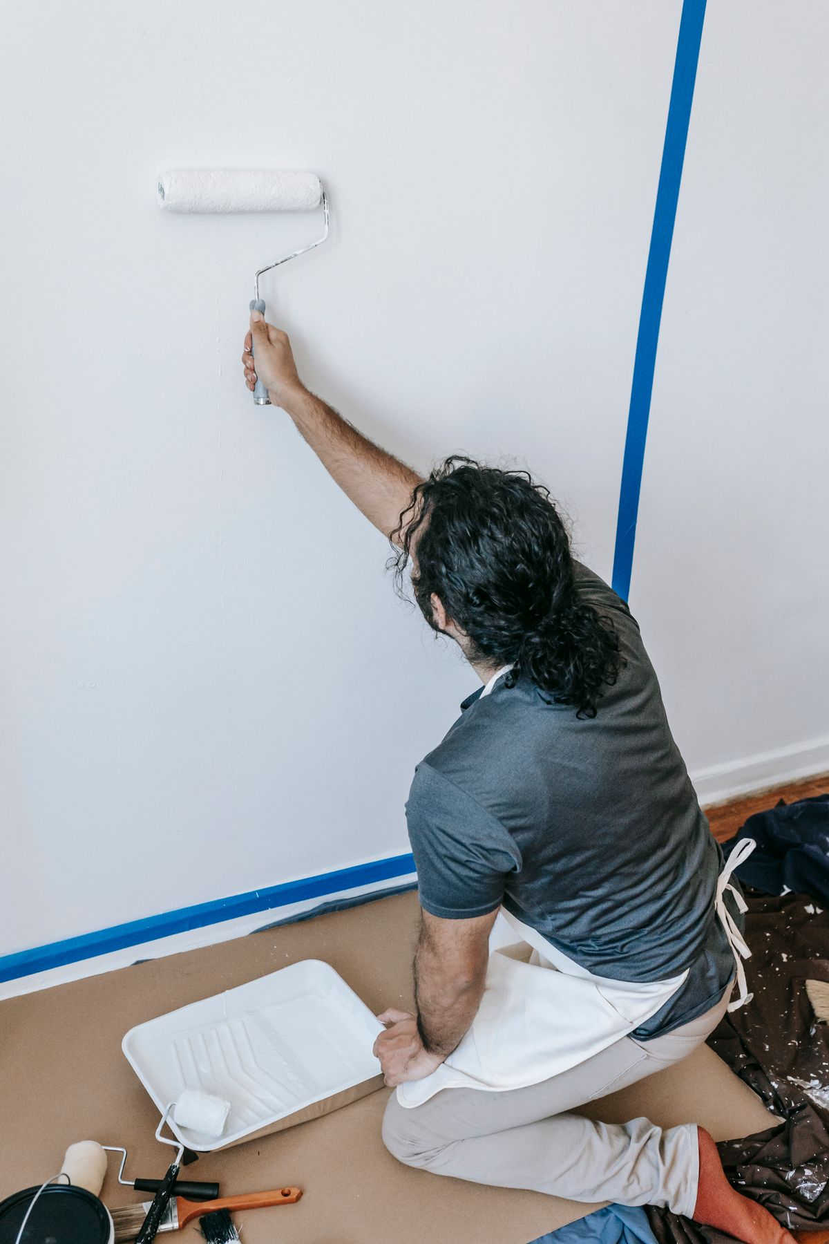 A painter kneeling and rolling white paint onto an interior wall