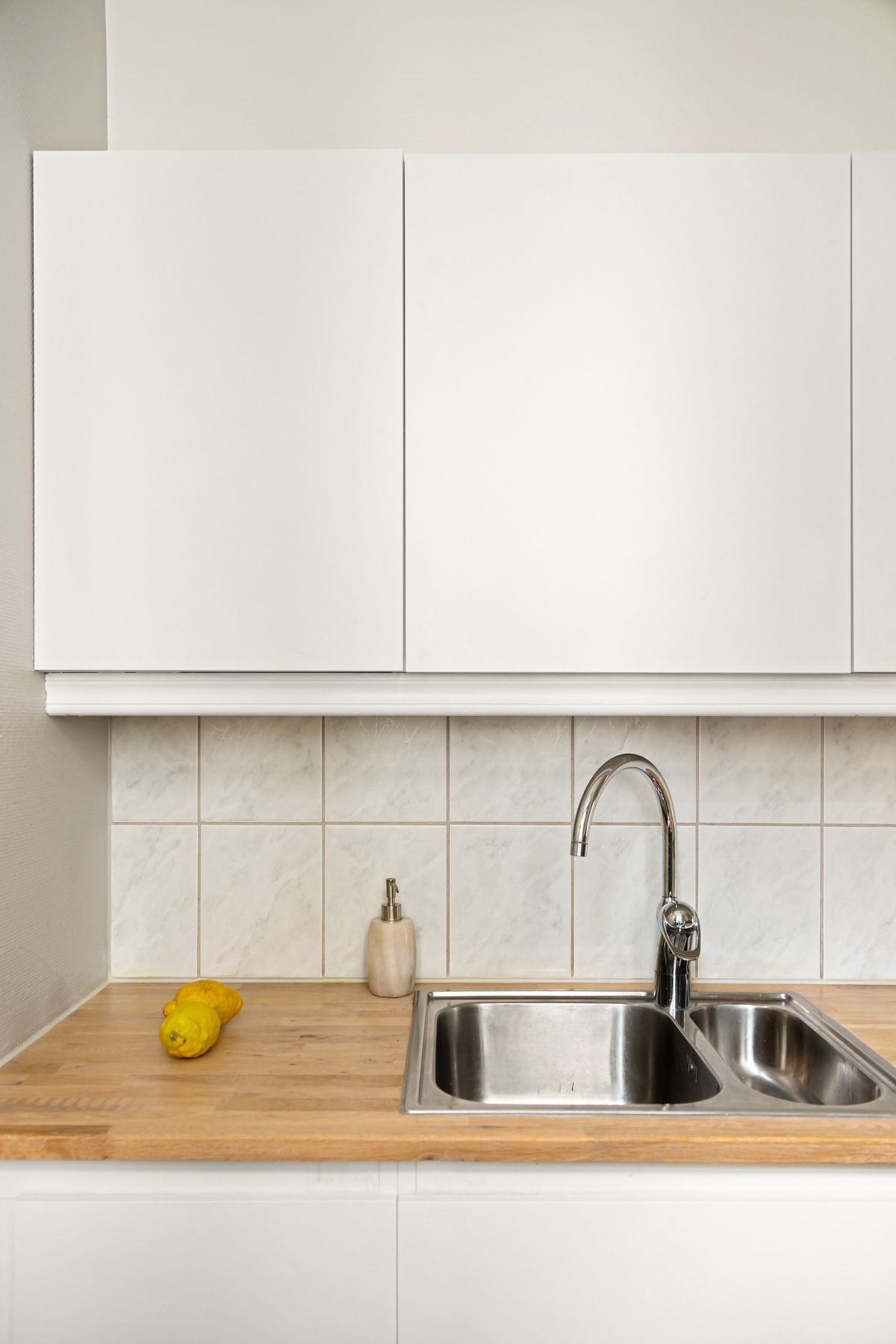 A bright white kitchen with a stainless steel sink and wood counter